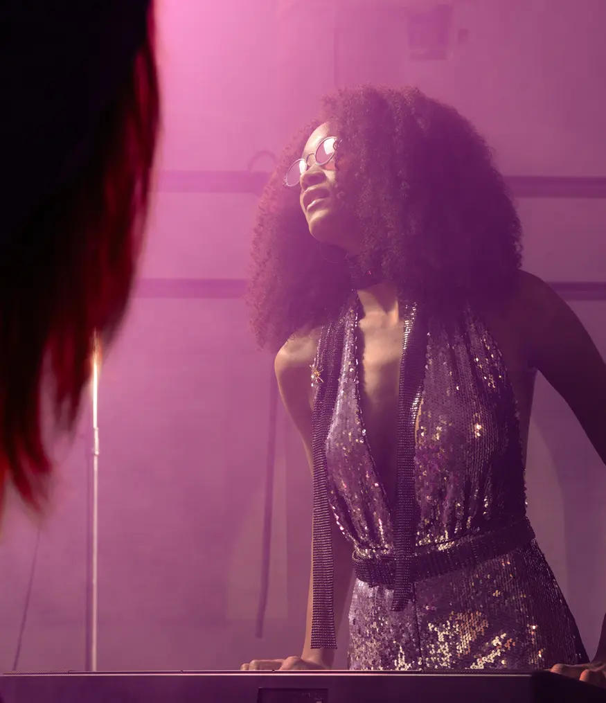 a woman bathed in pink light wearing sunglass and a sequined outfit