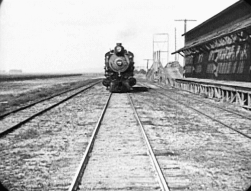 a black and white video looking straight down tracks to the front of a locomotive as it approaches