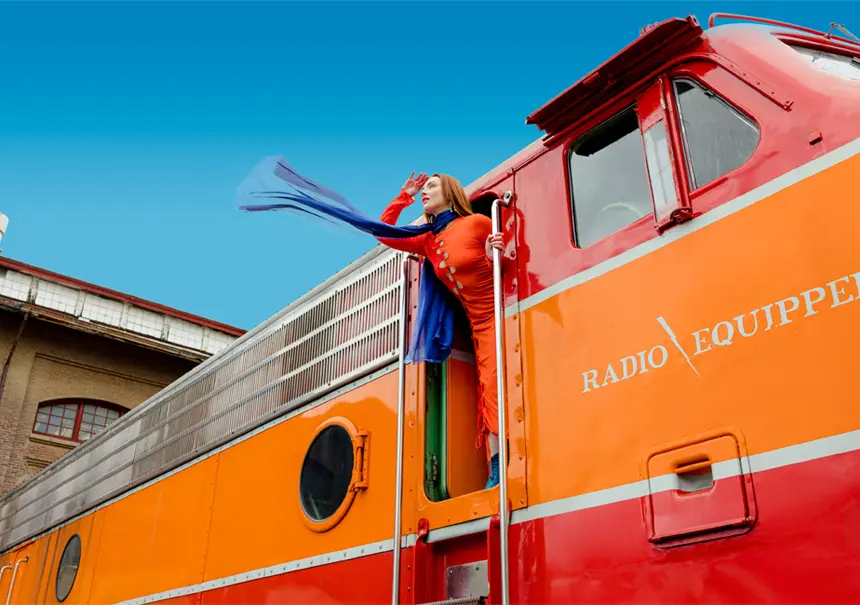 A woman wearing a red dress and purple scarf leaning out of a red locomotive