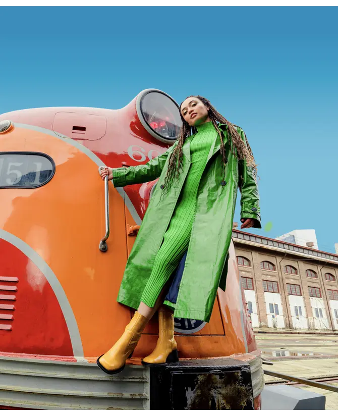 a woman in a green dress and jacket hanging off the front of a red locomotive