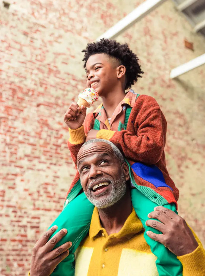 an elderly man holding a young boy with an ice cream cone on his shoulders