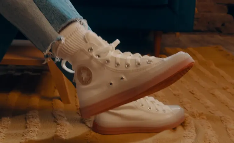 a close up photo of a feet wearing white converse hightops