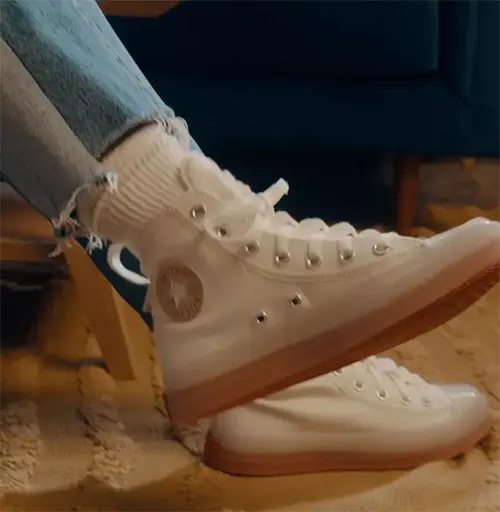 a close up photo of a feet wearing white converse hightops