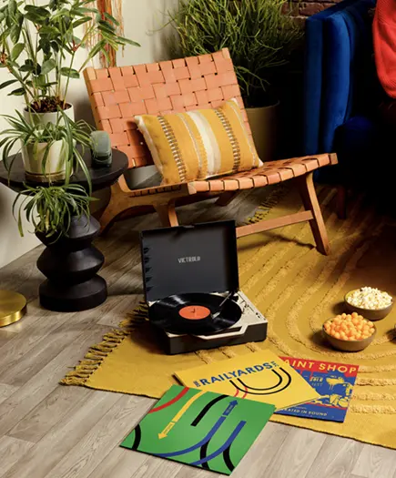 a photo an interior room containing an orange chair and yellow rug with a record player sitting on the ground