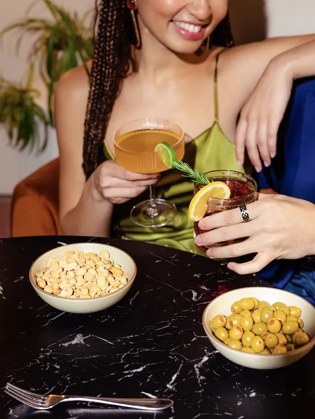 a smiling woman in a green dress toasting her drink with another person