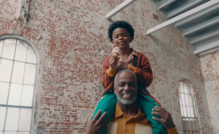 a photo of an elderly man holding a young boy with an ice cream cone on his shoulders