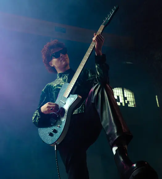 a man wearing a green shirt and black leather pants playing the guitar