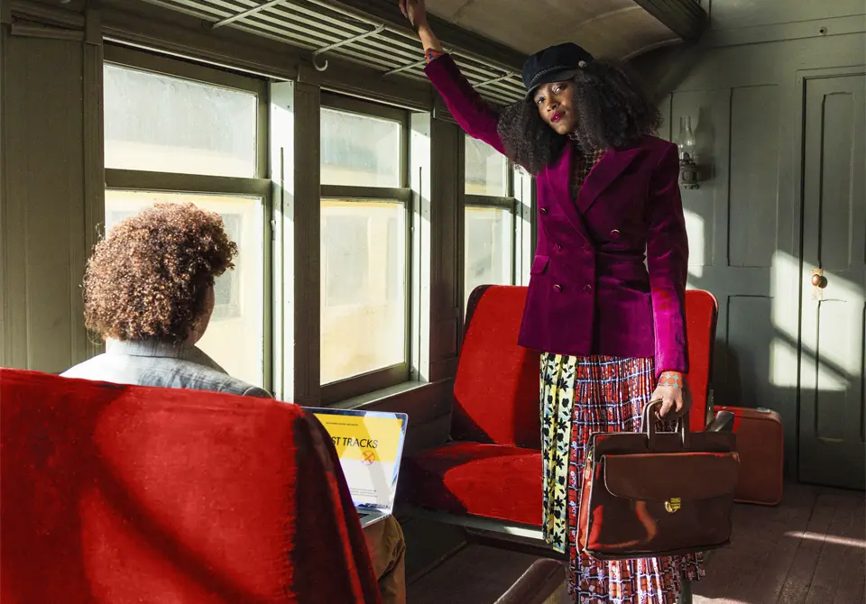 a woman wearing a purple jacket and holding a satchel standing inside an old passenger train car