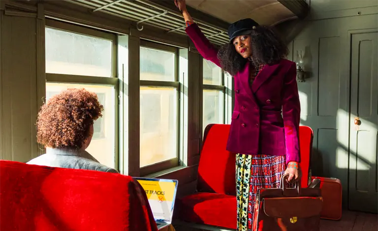 a woman wearing a purple jacket and holding a satchel standing inside an old passenger train car