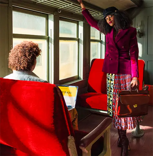 a woman wearing a purple jacket and holding a satchel standing inside an old passenger train car