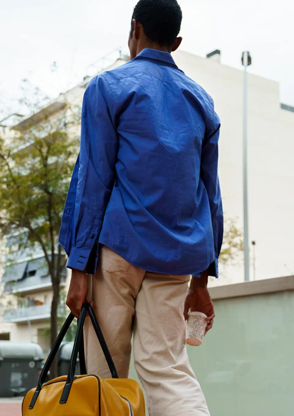 a photo of a man wearing a blue shirt and tan pants walking away from the camera