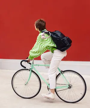 a person wearing a green sweater and white pants riding a bike in front of a red wall