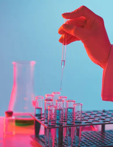 a photo of a hand using a pipette to drop liquid into test tubes