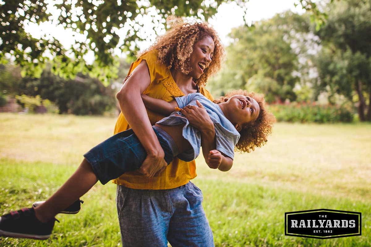A mom and her child play in the sun in a local park. Discover how the Railyards is using parks like this one as part of a green construction approach.