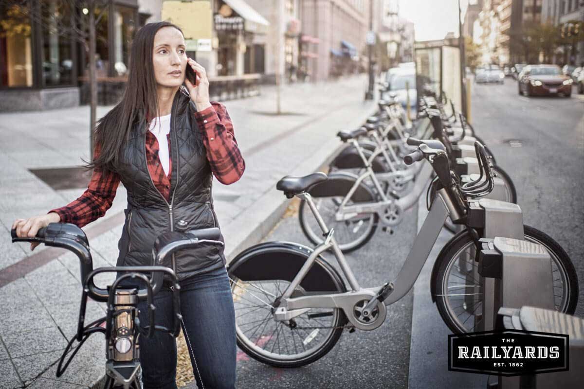 A woman with her bike in a downtown environment. Find out the 6 best cities for cycling in the US.